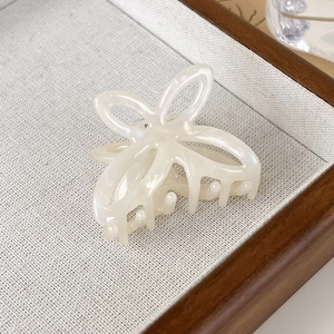 Detail shot of a pearlescent cream butterfly hair claw clip on a textured fabric tray