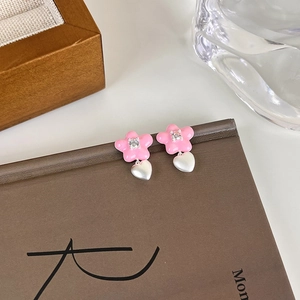 Détail de boucles d'oreilles fleur rose avec zircon et breloque coeur blanc mat