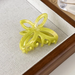 Close-up of bright yellow acetic acid butterfly hair claw with marble texture on wood tray