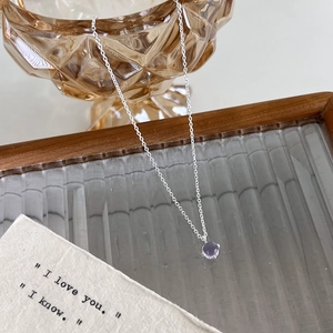 Gros plan d'une chaîne en argent avec pendentif en cristal violet sur un plateau en verre