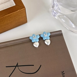 Détail de boucles d'oreilles fleurs bleu clair avec cœurs argentés et cristaux