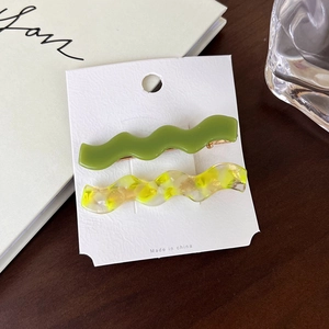 Detail view of wavy acetate hair clips in green and marble white on a display card