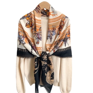 Retro horse carriage pattern scarf with fringe edges draped over a beige knit top