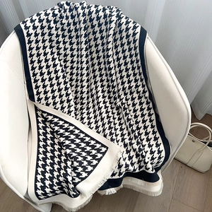 Classic black and white houndstooth scarf with tassels draped on a white chair