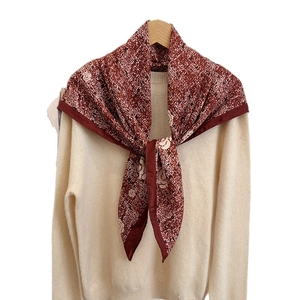 Luxurious camellia print square silk scarf in burgundy displayed on a beige sweater