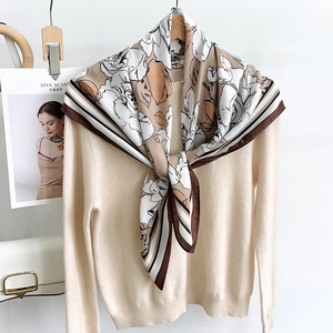 Détail d'un foulard en soie à imprimé rose porté sur un pull en maille beige