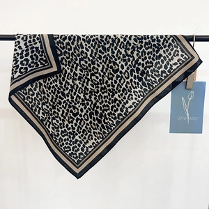 Elegant leopard print square scarf with contrast border hanging on a metal rack