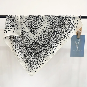 Fashionable leopard print silk square scarf in beige and black displayed on a hanger