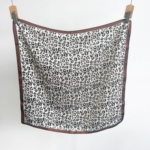Close-up of leopard print square silk scarf with brown edges hanging on a white backdrop