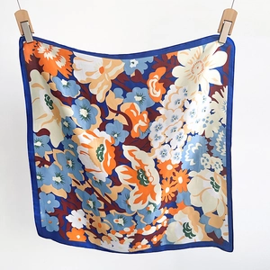Détail d'un foulard carré en soie à imprimé floral avec des fleurs orange et bord bleu