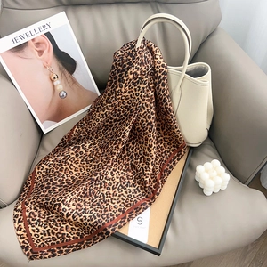 Detailed view of leopard print satin square scarf with brown border on a leather sofa