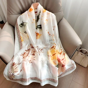 Elegant floral print long silk scarf with vintage borders draped on a leather chair