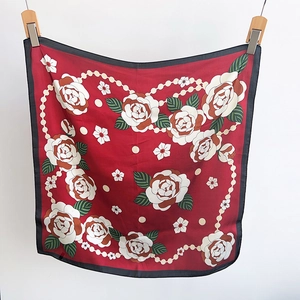 Détail du foulard en soie rouge avec imprimés de roses blanches et motifs de perles