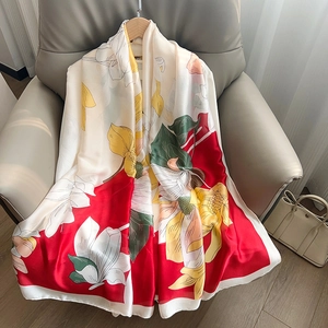 Elegant magnolia floral print silk scarf in red and cream displayed on a leather chair