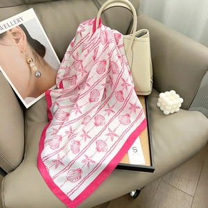 Pink and white ocean-themed silk scarf with seashell patterns on a luxury sofa