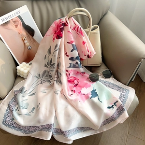 Detailed close-up of floral print silk scarf featuring pink blossoms and fret pattern edges