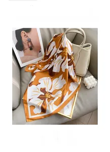 Detail of floral silk scarf in orange and cream displayed on a stylish beige handbag