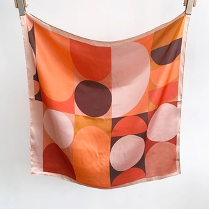 Detailed view of silk-like square scarf featuring geometric circles and warm color blocking