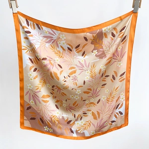 Gros plan d'un foulard en satin aux bordures oranges et motifs floraux plissé avec soin