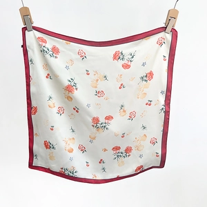 Detail view of floral silk scarf featuring red roses, cherries and contrasting red borders