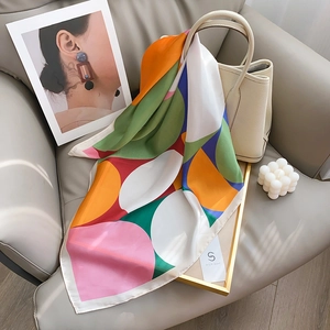 Silk-textured square scarf with colorful geometric patterns draped on a luxury sofa