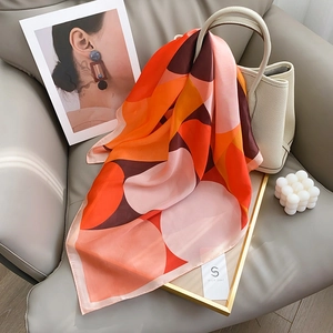 Polka dot geometric silk square scarf in orange and brown draped over a white luxury handbag