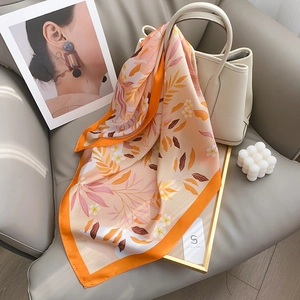Élégant foulard en soie à fleurs orange et beige drapé sur un sac à main blanc