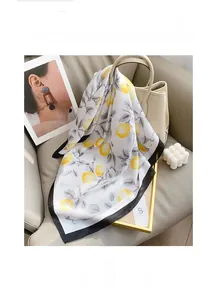 Détail d'un foulard carré en soie avec motif citron et bordure noire sur canapé