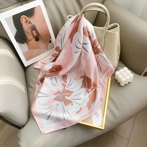 Elegant floral print silk scarf in soft pink draped over a beige bag for spring style