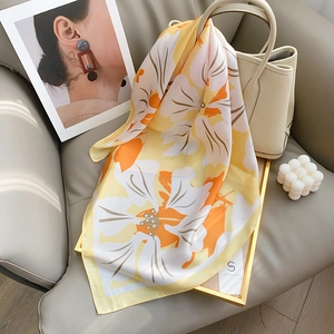 Floral print silk square scarf in orange and yellow draped over a white luxury handbag