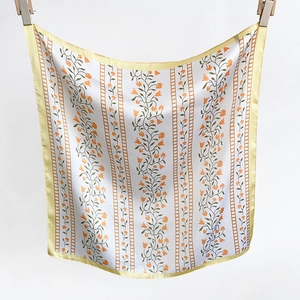 Detail of floral silk square scarf with orange vine patterns and yellow satin edges