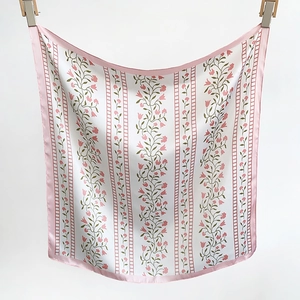 Detail view of small pink floral patterns and green vines on a white silk neck scarf