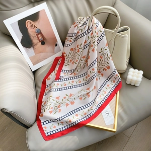 Floral silk square scarf with red border draped over a sofa in elegant setting