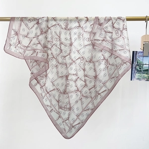 Close-up of lightweight square scarf with geometric patterns on a gold display rack