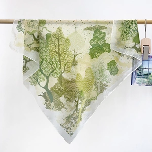 Détail d'un foulard en soie avec imprimé de forêt verte suspendu à une barre en bois