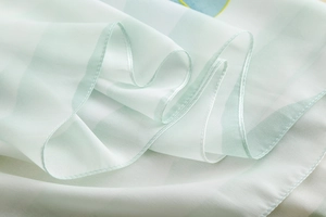 Gros plan d'une écharpe en mousseline rayée vert clair avec ourlet roulé et texture