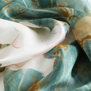 Elegant silk scarf featuring lotus patterns in teal and ivory with a smooth glossy texture