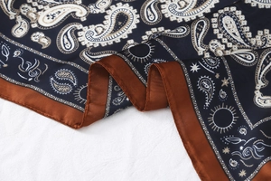 Detail of silk-textured paisley square scarf with deep blue pattern and copper satin edge