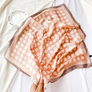 Détail d'un foulard en satin rose orangé à pois blancs avec bordure marron
