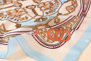 Detailed view of satin print scarf featuring golden chains and blue borders on silk fabric