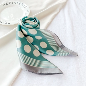 Détail d'un foulard en soie sarcelle à pois blancs avec bordure rayée sur tissu blanc