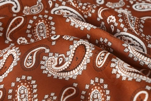 Macro shot of silk paisley pattern fabric in burnt orange with premium glossy texture