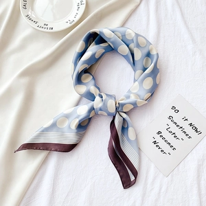 Détail d'un foulard en soie bleu clair à pois blancs avec bordure contrastée marron chic