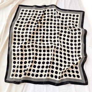 Détail d'un foulard carré en soie avec pois noirs et bordure rayée sur tissu blanc