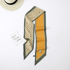 Detail of a green and yellow silk scarf with a B-letter pattern and a summer straw hat