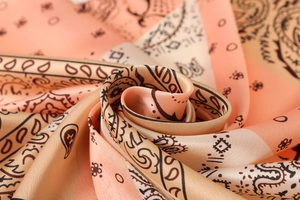 Macro view of silky peach paisley satin scarf showing fabric texture and soft luster