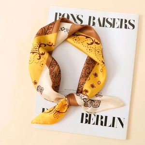 Detailed close-up of a satin paisley scarf tied over a magazine with yellow and brown tones