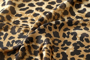 Close-up of silk-like leopard print fabric with ginger yellow base and soft texture
