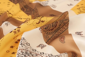 Detailed macro view of paisley pattern on silky satin scarf with yellow and ivory tones