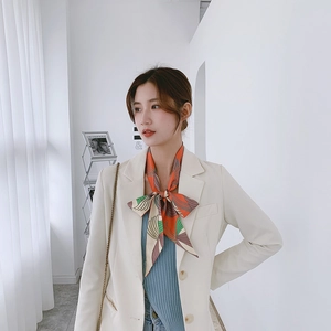 Detail of floral silk scarf tied in a bow on a model wearing an ivory blazer